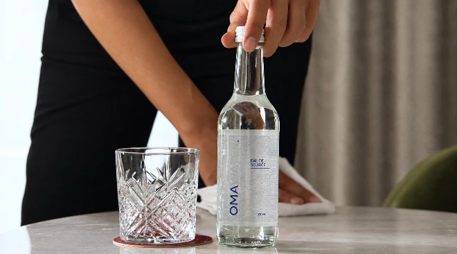 Bouteille en verre OMA Water servie au bar avec un verre taillé